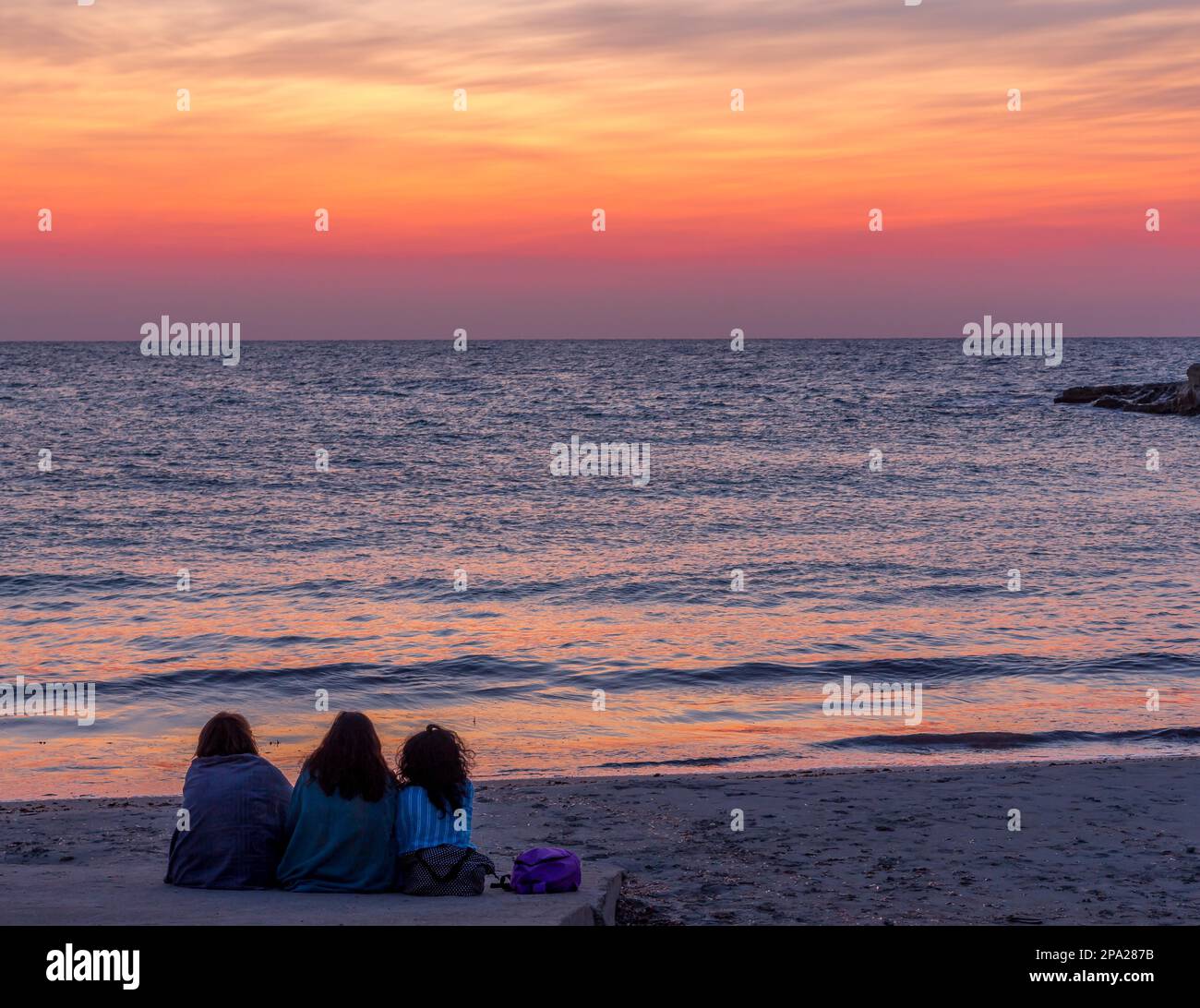 Tre donne in attesa dell'alba di fronte al mare (Puglia) (Sud Italia). Concetto di amicizia, viaggio e avventura Foto Stock