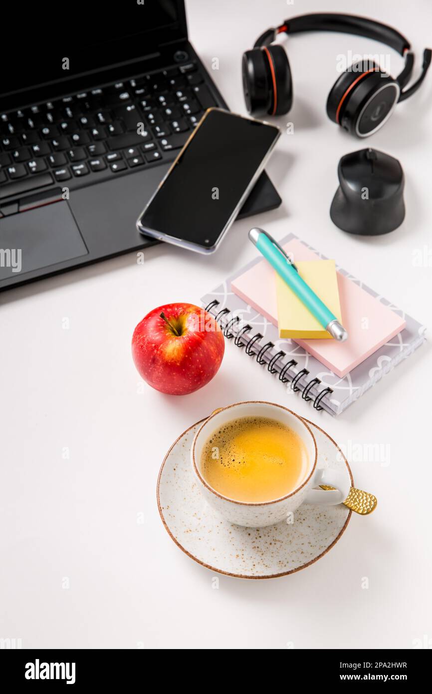 Posto di lavoro e scrivania con caffè, computer portatile, mela, cuffia e smarthpone. Piatto in tonalità nera Foto Stock