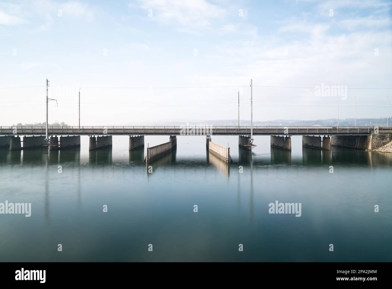 Un ponte di cemento sull'acqua con una linea ferroviaria e una strada che corrono in parallelo e un passaggio per barche e navi sotto sul lago di Zurigo vicino Rapperswil Foto Stock