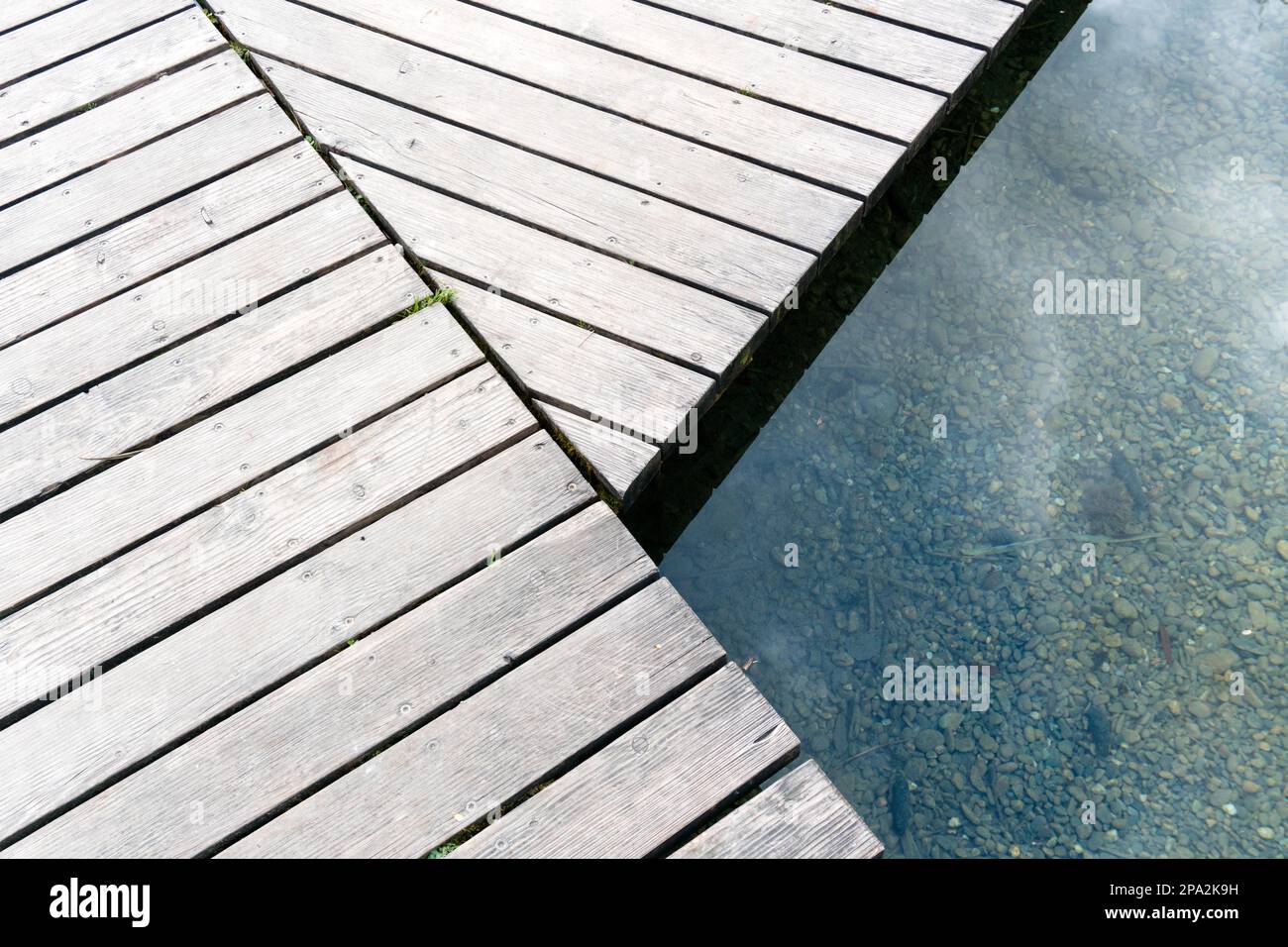 Lungo e tortuoso molo di legno sul lungomare, su un chiaro lago di montagna blu scuro da vicino Foto Stock