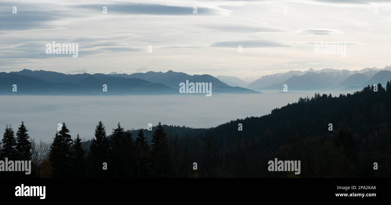Rolling creste di montagna in un cielo chiaro e nebuloso con la foresta di colore autunno in primo piano e molte montagne coperte di neve dietro nella valle del Reno di Foto Stock