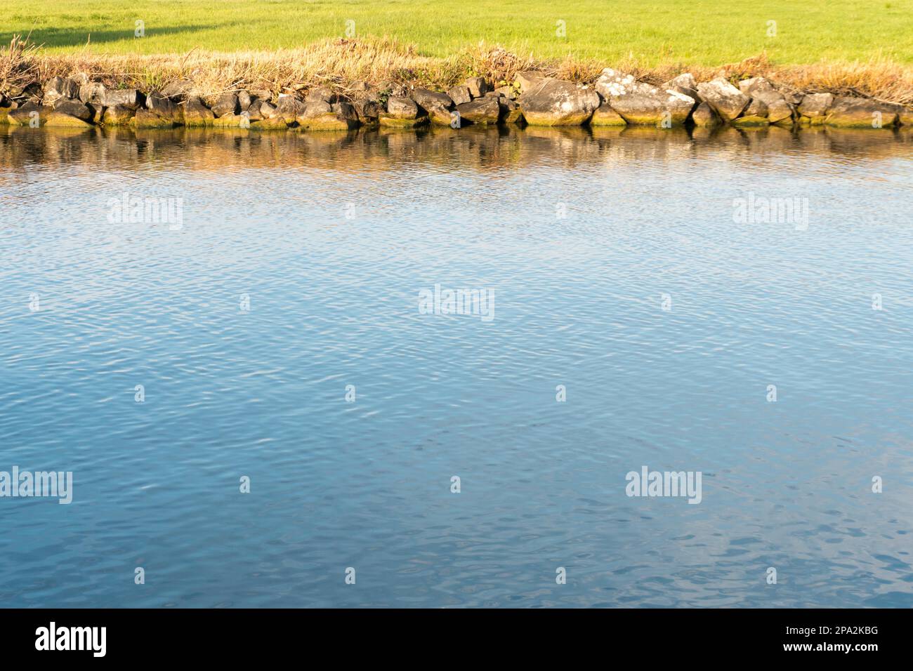 Canale blu profondo sul lago di Zurigo in Svizzera vista astratta con acqua e bordo roccioso del canale e lussureggiante erba verde dietro Foto Stock