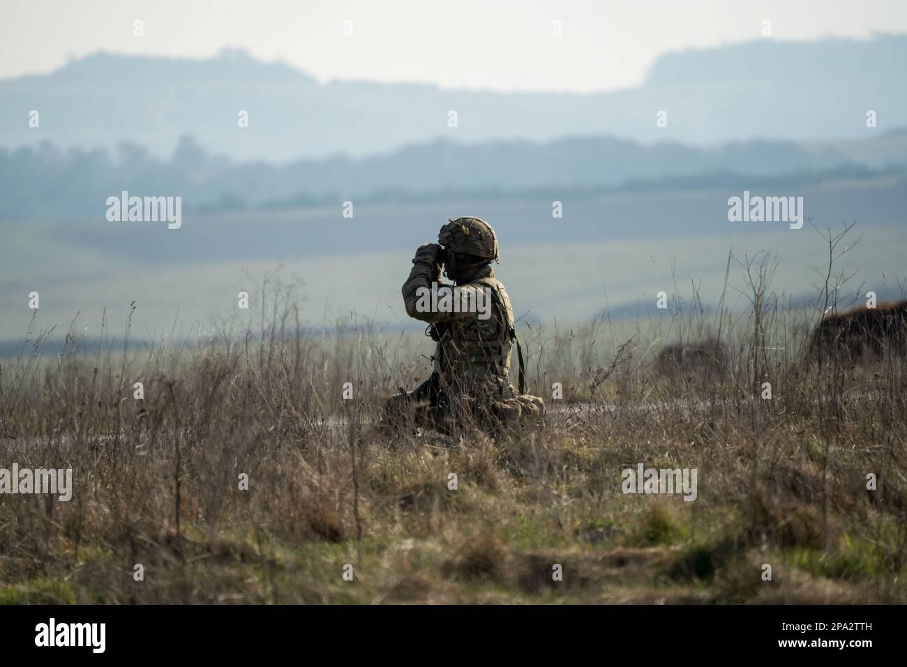 Soldato di fanteria dell'esercito britannico che usa binocoli per scannerizzare le minacce nemiche, l'esercizio militare, Wiltshire UK Foto Stock