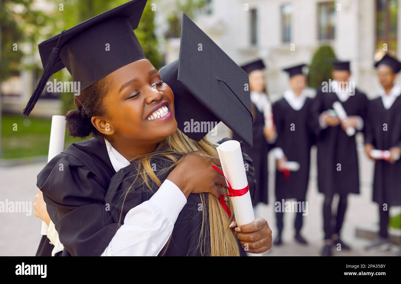 Felice ragazza studentesca afro-americana che abbraccia la sua amica universitaria il giorno della laurea Foto Stock