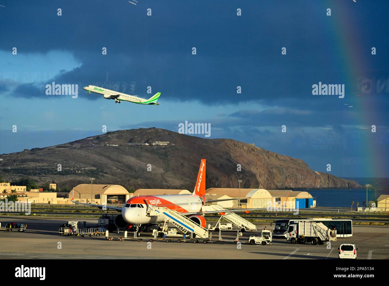 Osservare gli aeroplani dall'interno del terminal con uno a terra, un altro in aria con l'arcobaleno, l'Aeroporto di Gran Canaria Foto Stock