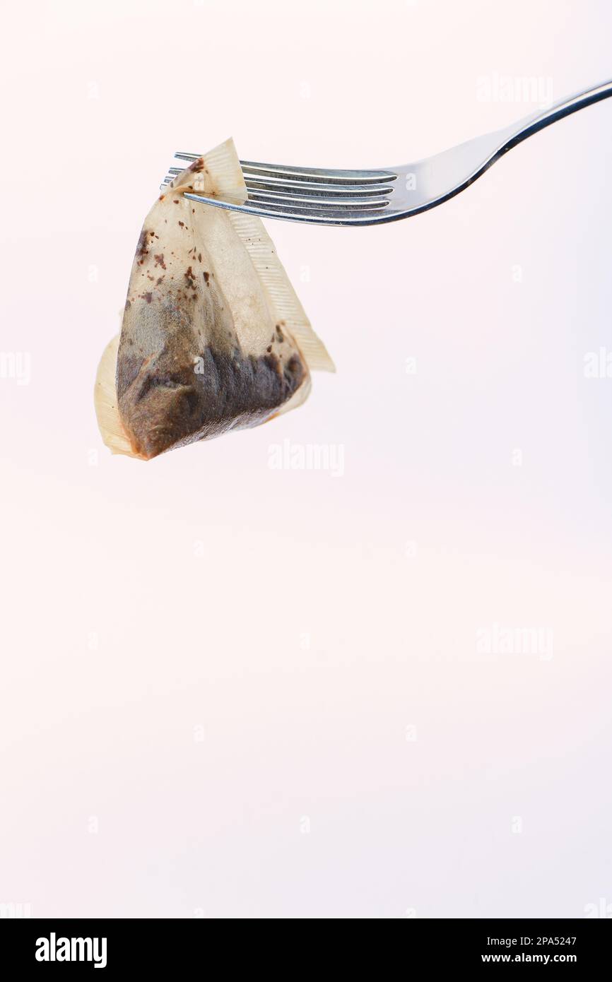 Borsa da tè triangolare usata appesa a una forchetta contro uno sfondo bianco. Il sacchetto del tè è punte di PG biodegradabili della pianta non ha basato la plastica. Foto Stock