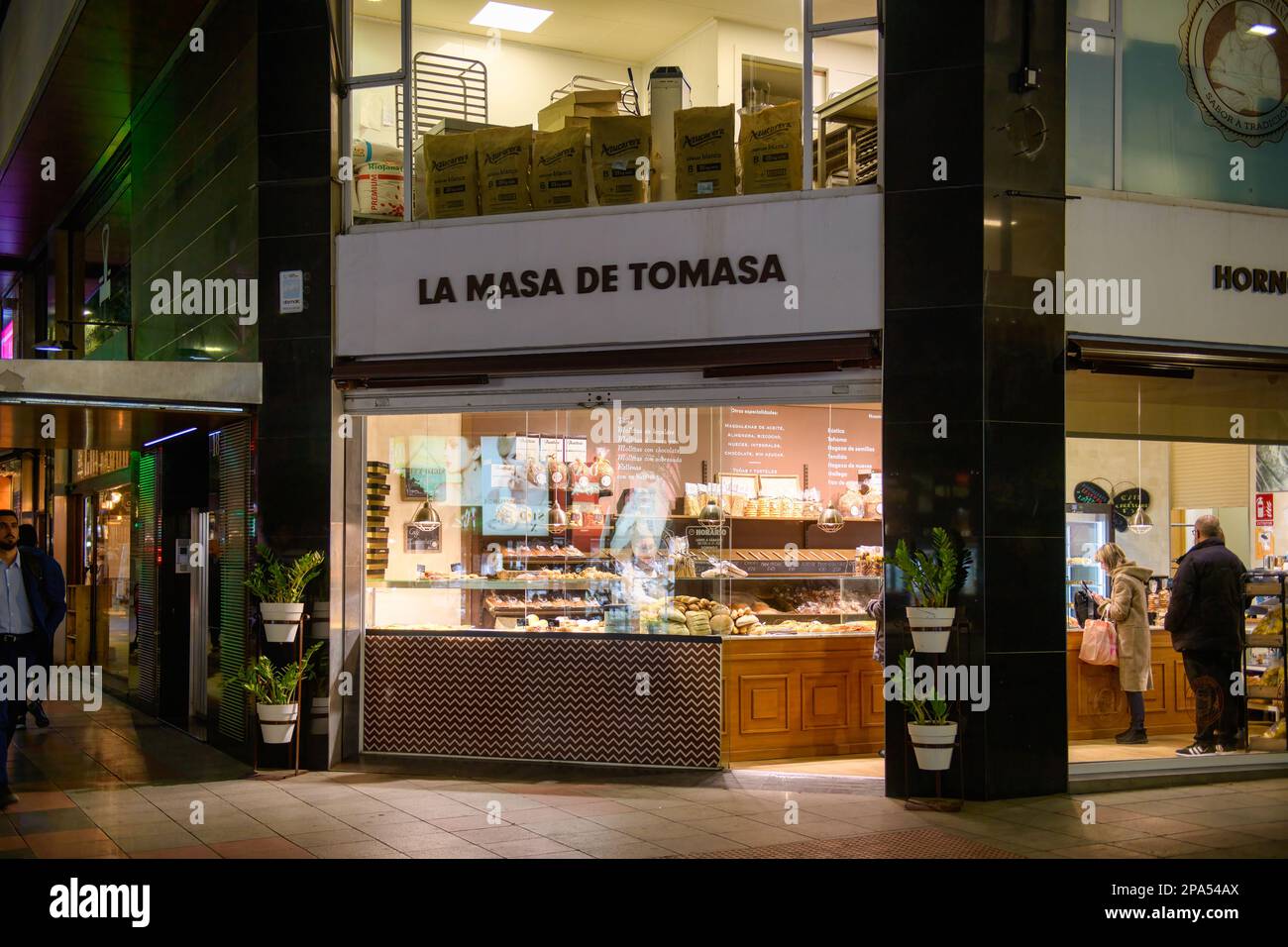 La gente compra il pane in un commercio di franchising denominato la Masa de TomasaScene della città di Alicante durante la notte in Spagna. Foto Stock