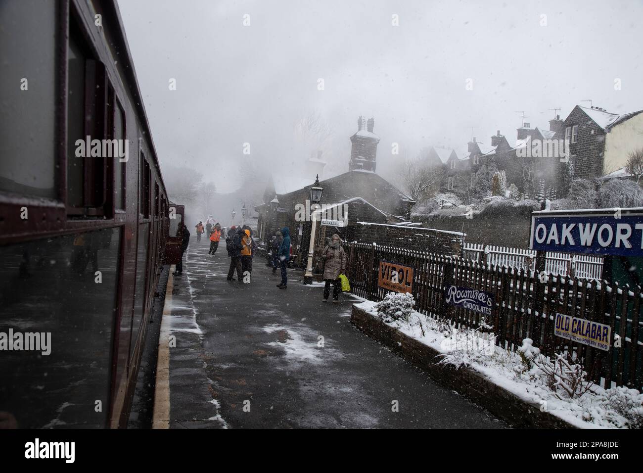 Il vapore e la neve nuvolano la stazione ferroviaria di Oakworth mentre i passeggeri saliranno a bordo e partiranno sulla ferrovia patrimonio della Worth Valley durante la settimana di Steam Gala Foto Stock