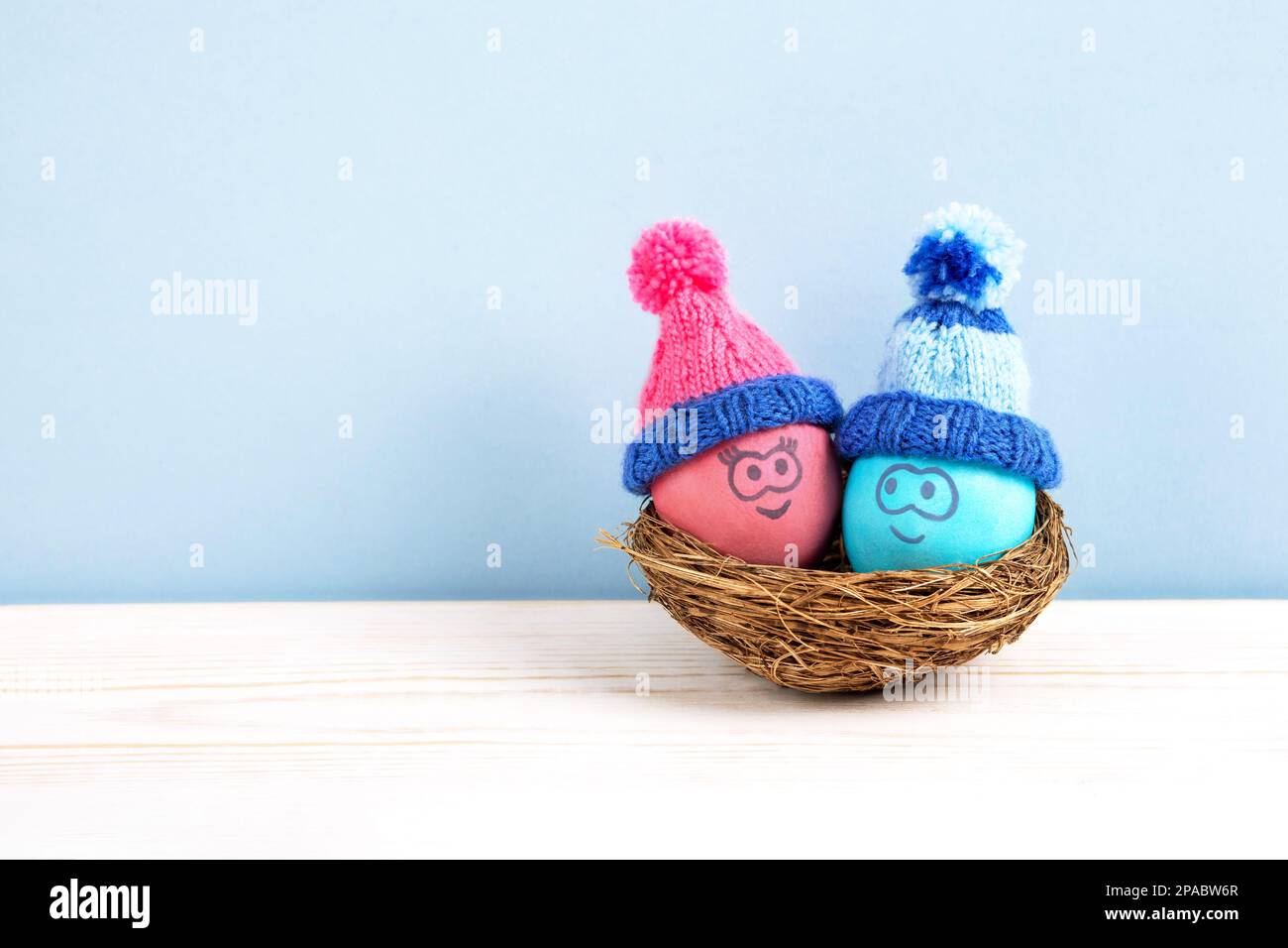 Due uova di Pasqua con volti divertenti e cappelli accovacciati in un nido decorativo di sisal su un tavolo di legno. Buon concetto di Pasqua. Biglietto d'auguri. Foto Stock