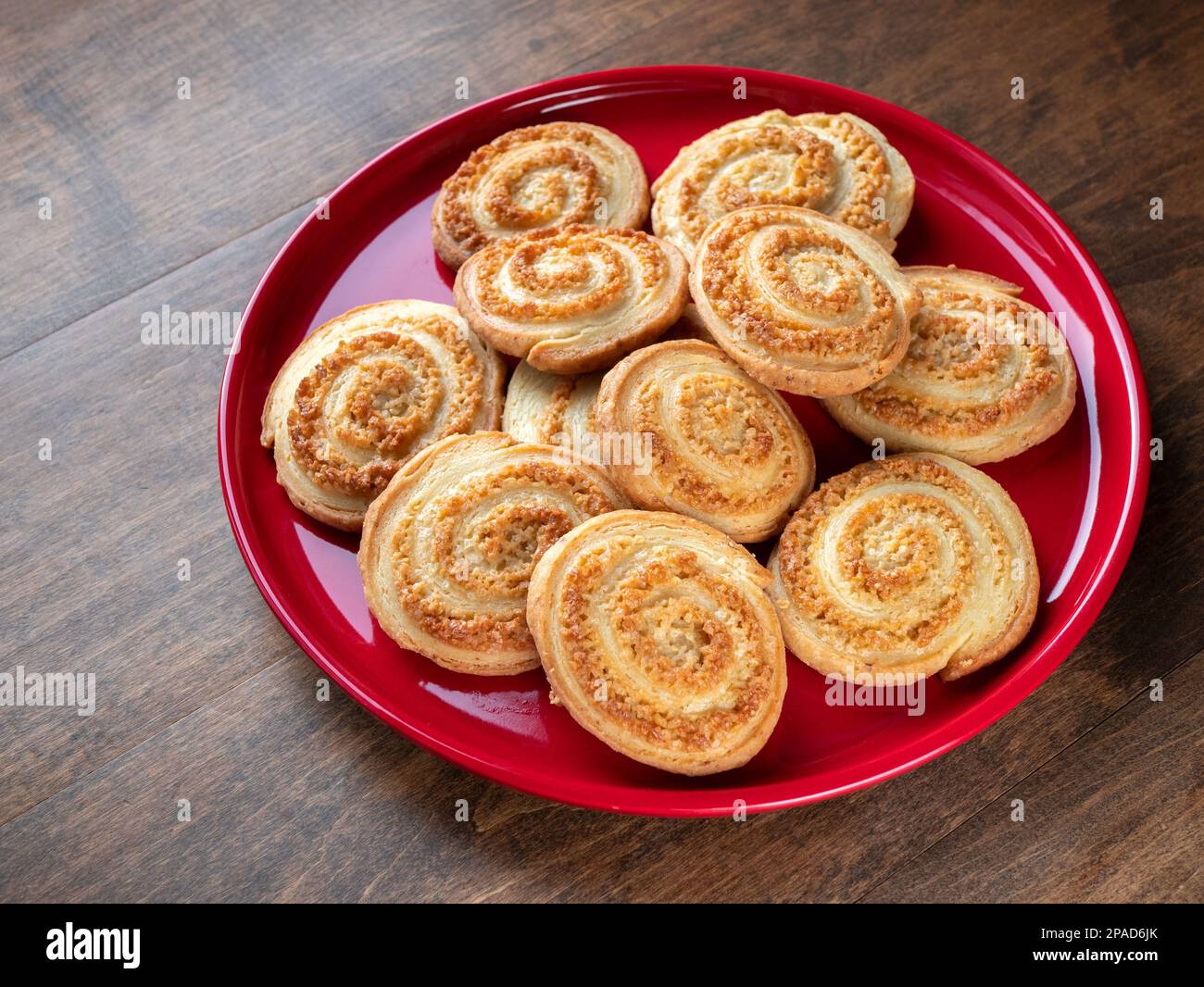 Biscotti freschi a forma di spirale su un piatto rosso su un tavolo di legno, messa a fuoco selettiva. Biscotti fatti in casa per dessert Foto Stock