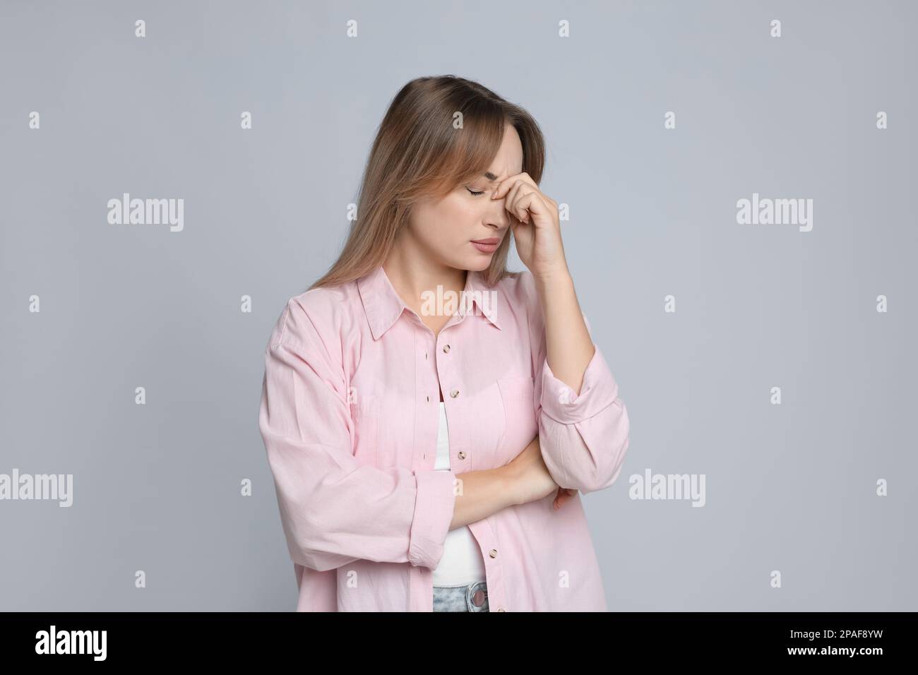 Giovane donna che soffre di mal di testa su sfondo grigio chiaro Foto Stock