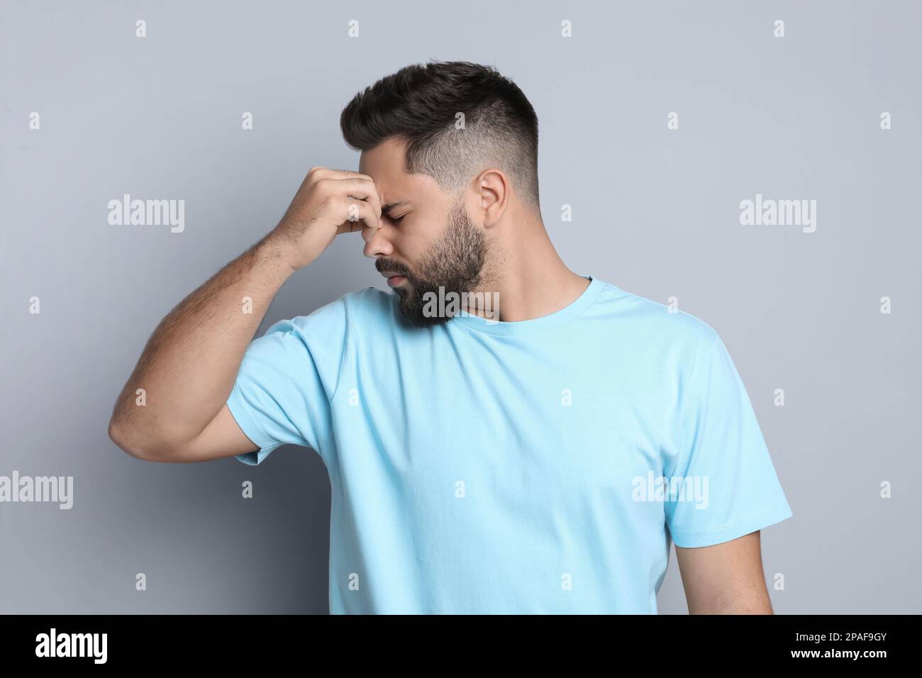 Giovane uomo che soffre di mal di testa su sfondo grigio chiaro Foto Stock