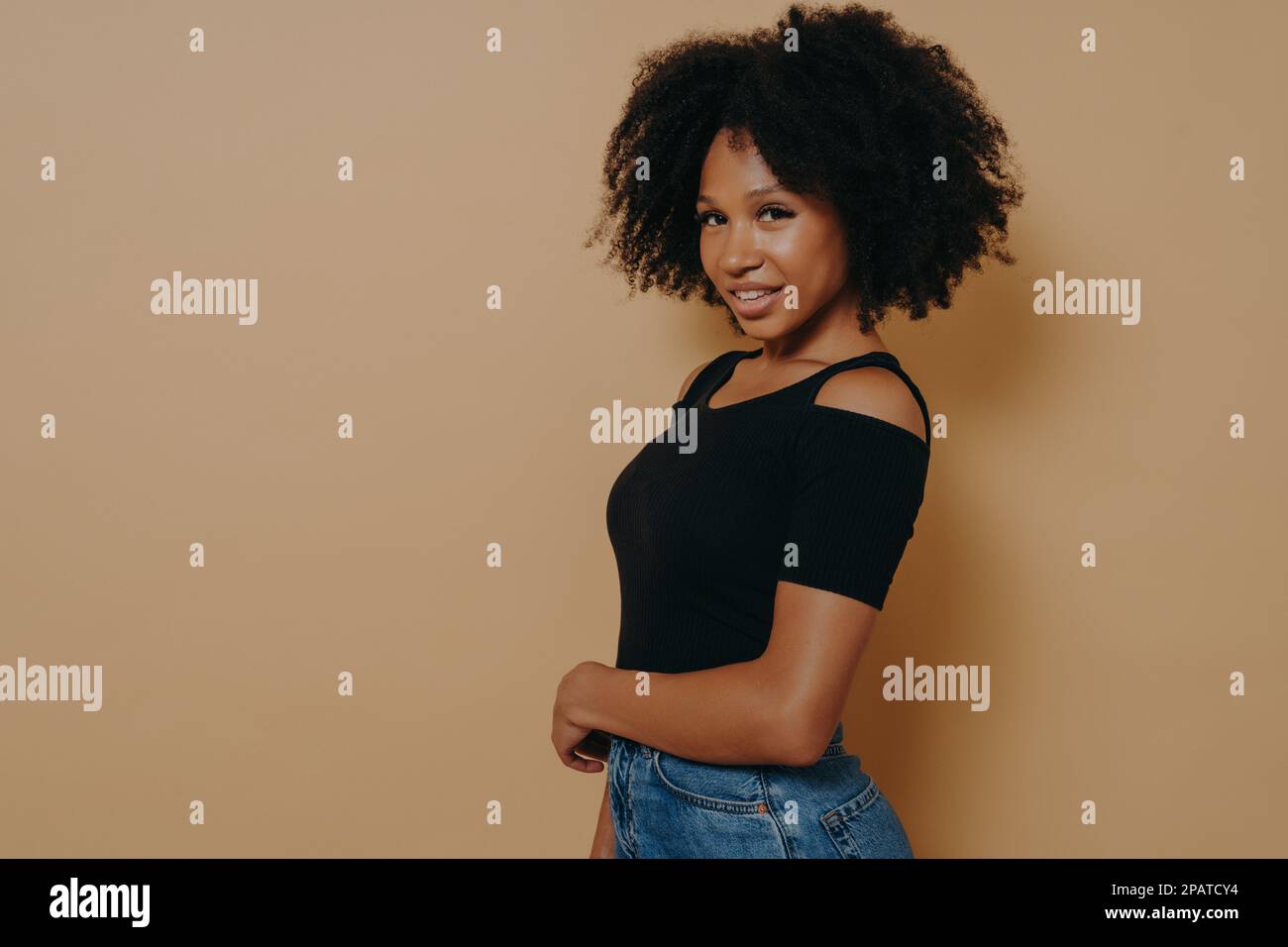 Profilo ritratto di bella ragazza afroamericana con sorriso beaming e labbra piene in abito casual isolato su sfondo beige scuro con poliziotto Foto Stock