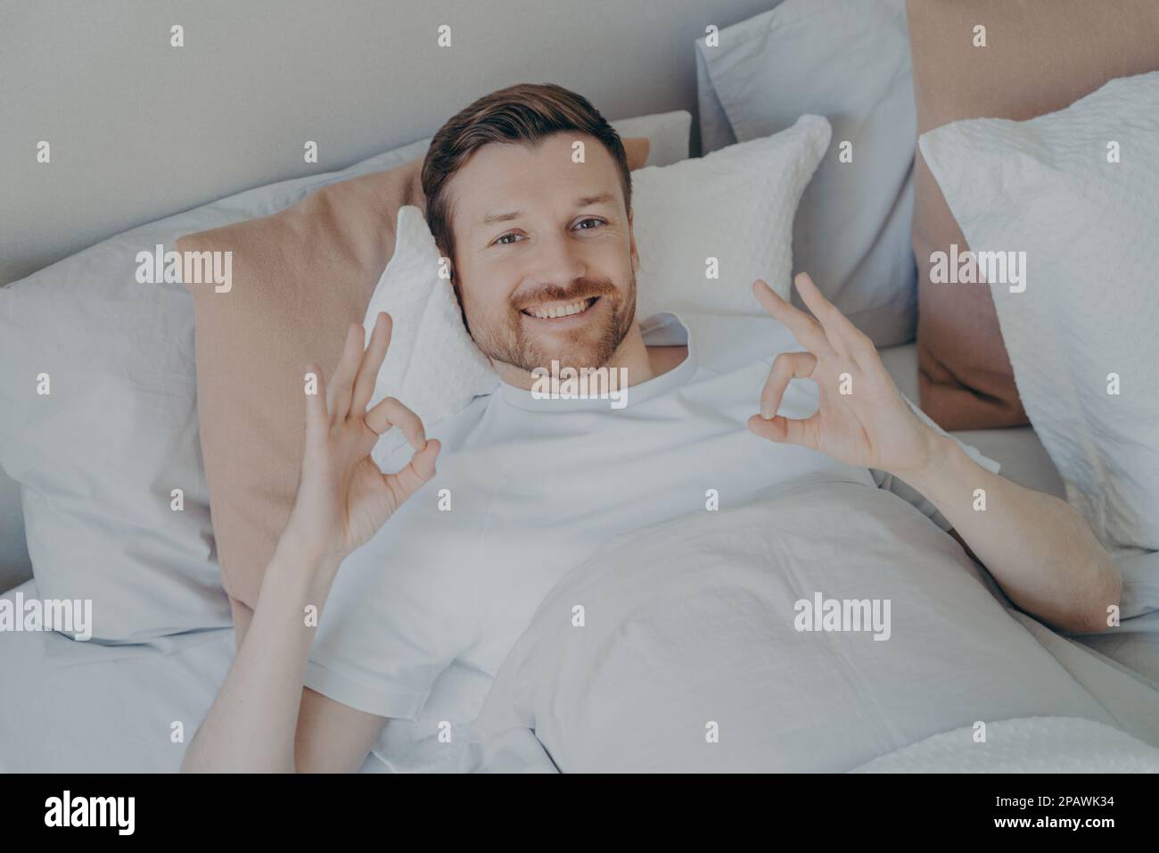 Rilassato giovane uomo bearded sdraiato nel suo letto dopo il risveglio di mattina presto, godendo il tempo libero mentre si soggiorna a casa il fine settimana, soddisfatto ragazzo Sho Foto Stock