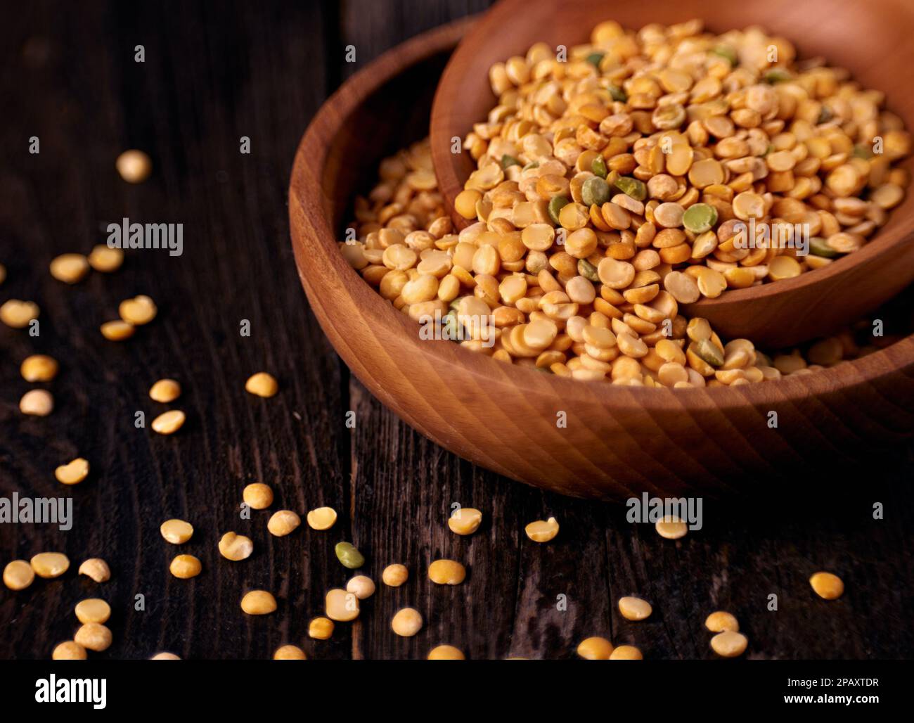 Due ciotole di legno con grani di piselli gialli asciutti su un tavolo di legno scuro Foto Stock