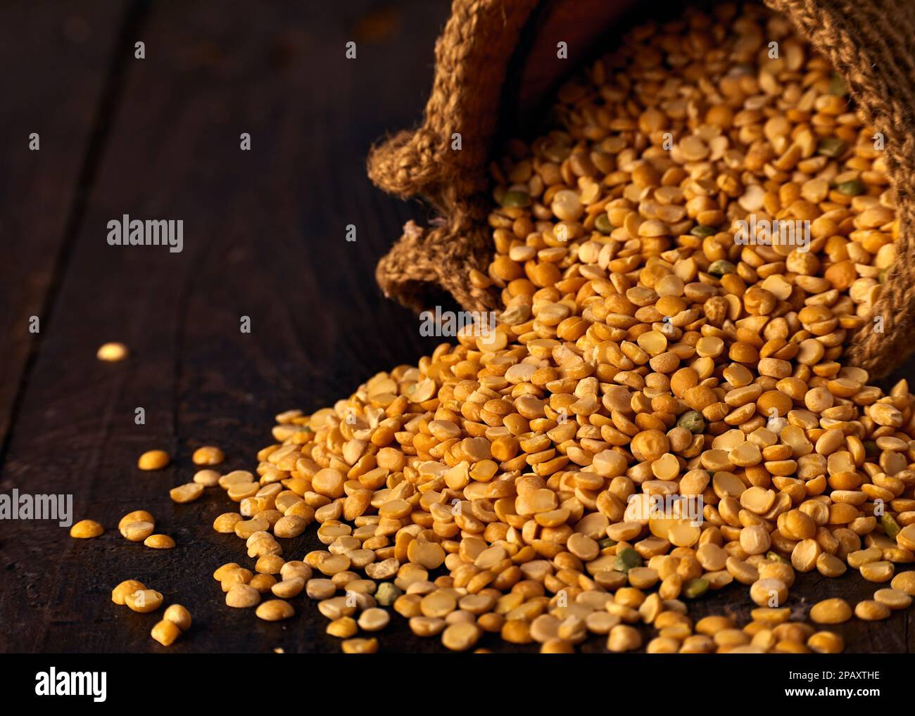 Grani di piselli gialli asciutti versati da un sacchetto di iuta su un tavolo di legno Foto Stock
