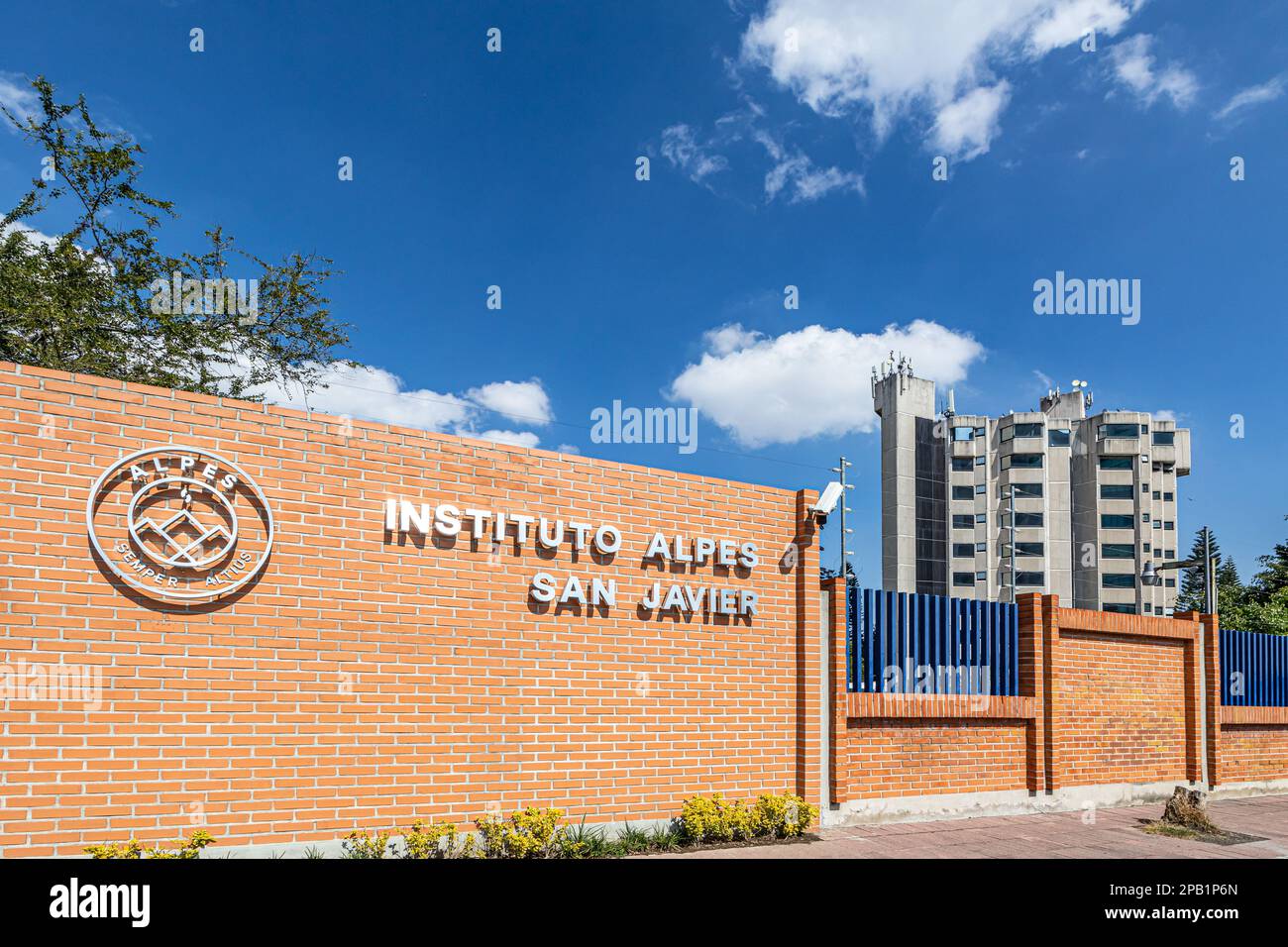 Zapopan, Jalisco Messico. Gennaio 1, 2023. Recinzione esterna in mattoni dell'Istituto Alpes San Javier contro un cielo blu, enorme edificio alto sullo sfondo, sole Foto Stock