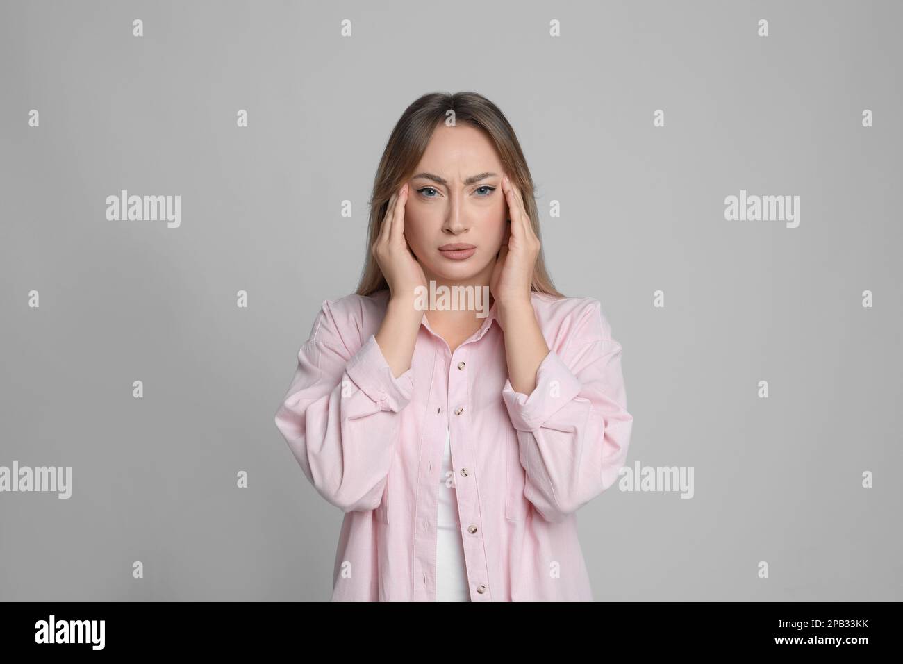 Giovane donna che soffre di mal di testa su sfondo grigio chiaro Foto Stock