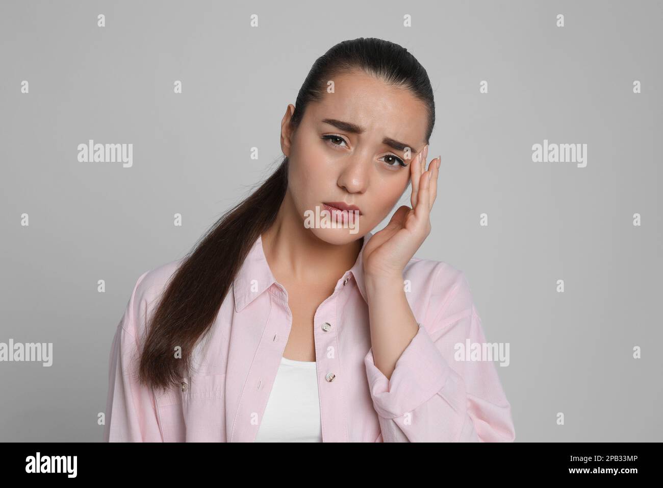 Giovane donna che soffre di mal di testa su sfondo grigio chiaro Foto Stock