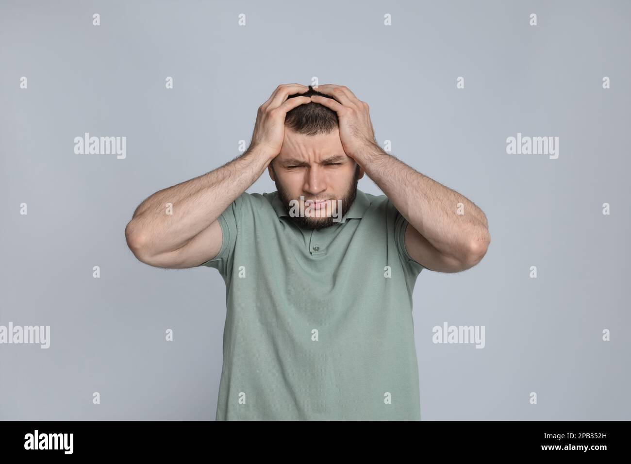 Uomo che soffre di mal di testa su sfondo grigio chiaro Foto Stock