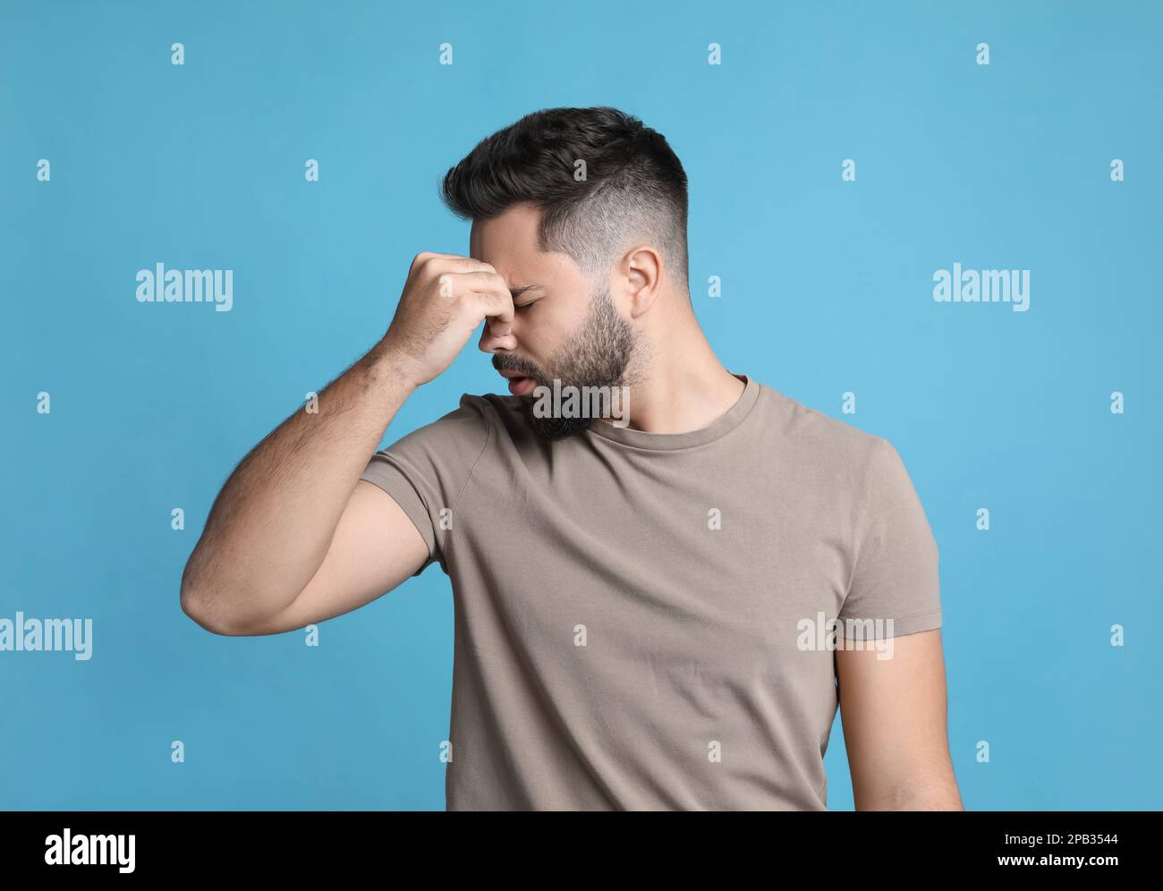 Giovane uomo che soffre di mal di testa su sfondo azzurro Foto Stock