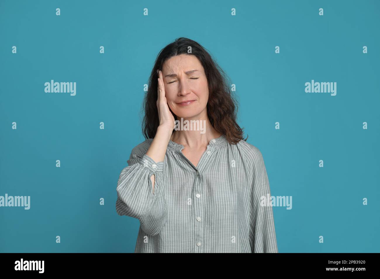 Donna matura che soffre di mal di testa su sfondo azzurro Foto Stock