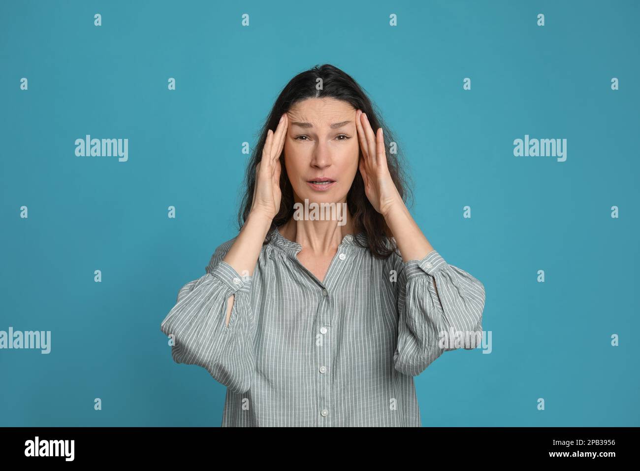 Donna matura che soffre di mal di testa su sfondo azzurro Foto Stock