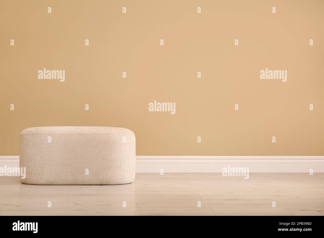 Elegante e confortevole pouf vicino alla parete beige per interni, spazio per il testo Foto Stock