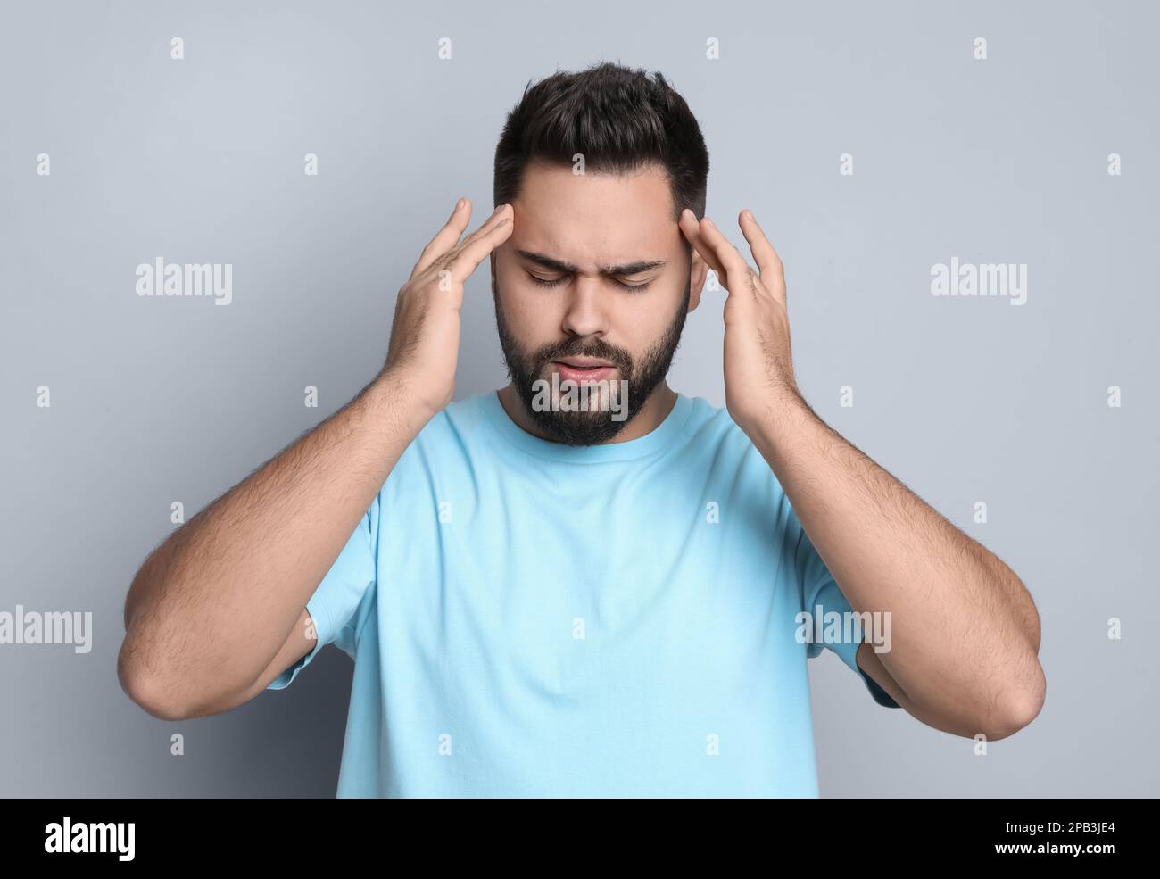 Giovane uomo che soffre di mal di testa su sfondo grigio chiaro Foto Stock