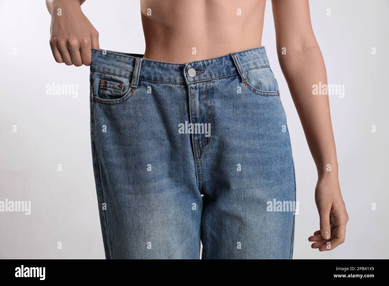 Donna skinny in jeans oversize su sfondo chiaro, primo piano. Concetto di perdita del peso Foto Stock