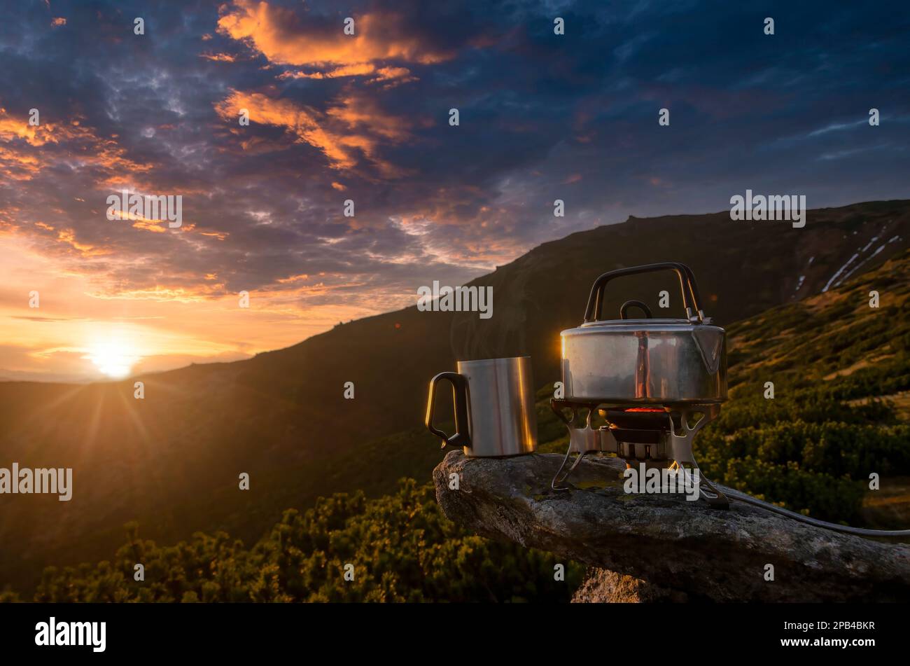 Tazza di tè caldo sulla cima della montagna. Incredibile tramonto di montagna con stufa turistica, teiera bollente e una tazza di tè. Simbolo di vacanza, libertà, all'aperto Foto Stock