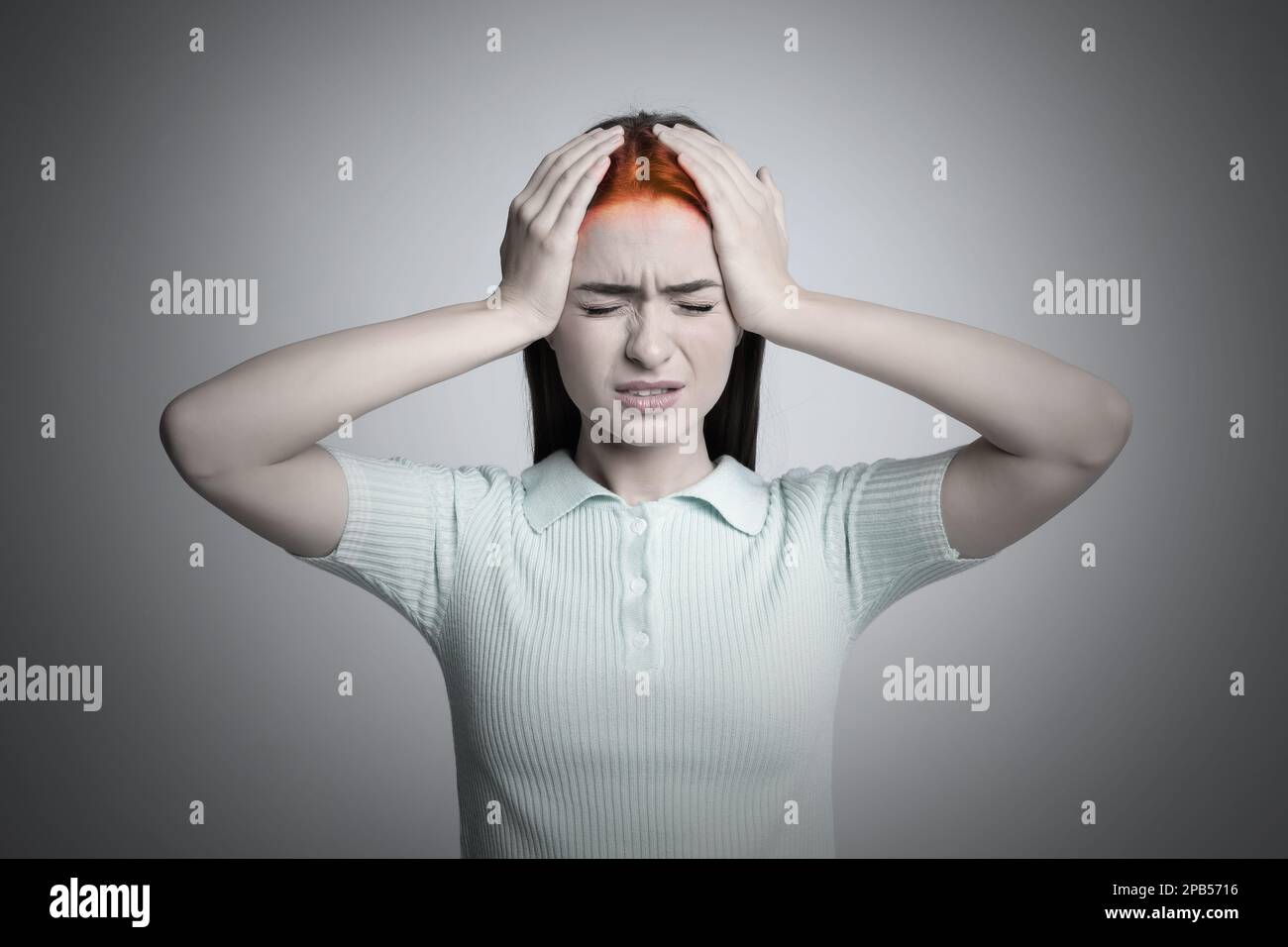 Giovane donna con mal di testa su sfondo grigio chiaro Foto Stock