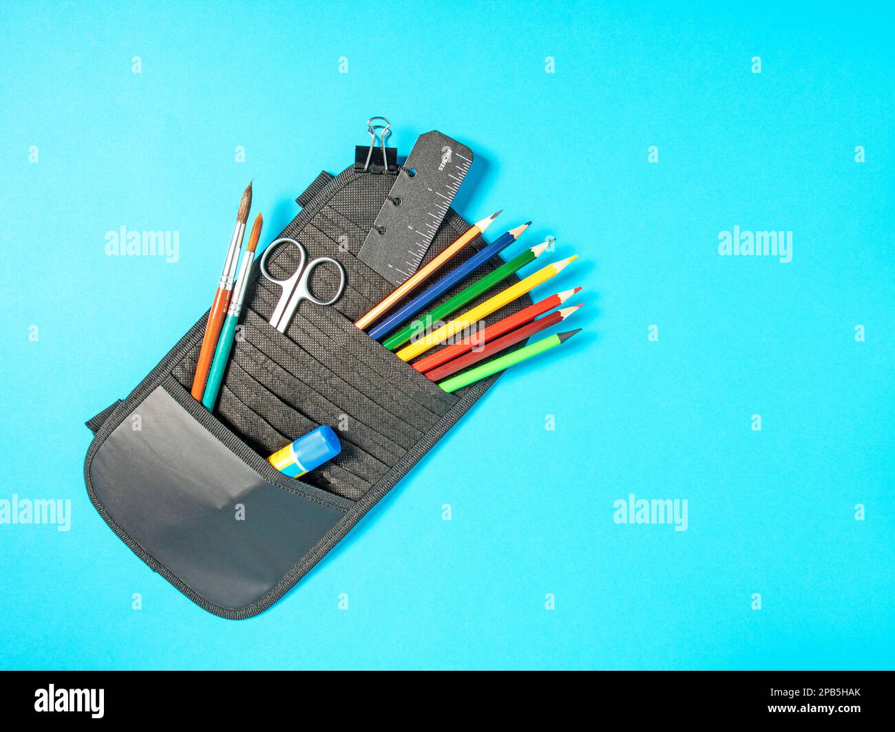 Busta per ufficio con cancelleria - matite colorate, pennelli, forbici, righello, su sfondo blu, vista dall'alto Foto Stock