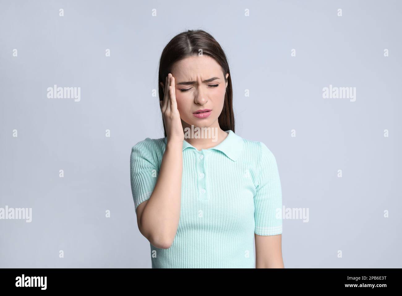 Giovane donna che soffre di mal di testa su sfondo chiaro Foto Stock