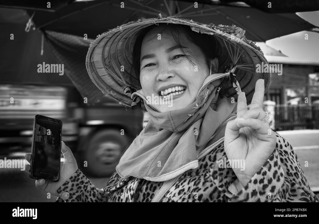 Una donna vietnamita che indossa un tradizionale cappello conico e che tiene in mano un telefono cellulare sorride e si posa per una foto in Tan Chau nel delta del Mekong a Vietna Foto Stock