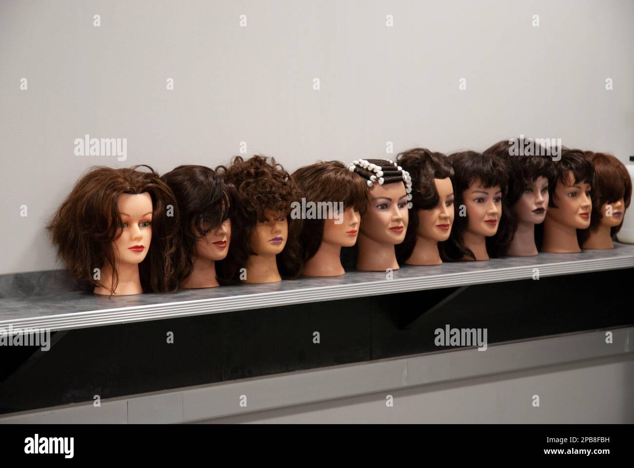 Una fila di teste di bellezza con vari acconciature , realizzate da studenti in una classe di cosmetologia. Per uso editoriale. Foto Stock