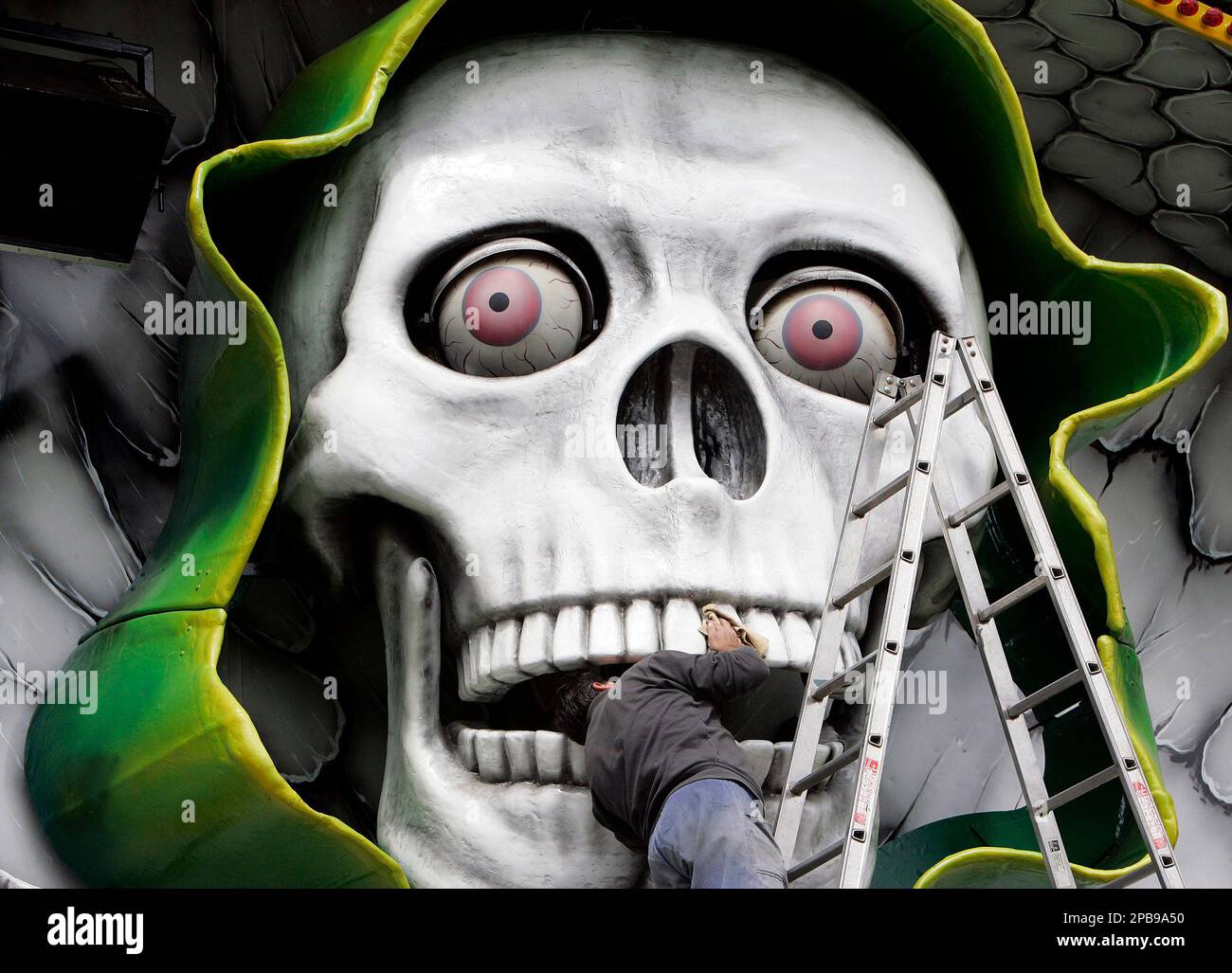 A man cleans the teeth of a giant skull decorating a ghost train ride at the Cranger Fair in Herne, western Germany, Tuesday, July 31, 2007. What started as a horse market in the 15th century has become one of Germany's biggest fairs with four million visitors expected in the ten days it runs. (AP Photo/Martin Meissner) Foto Stock