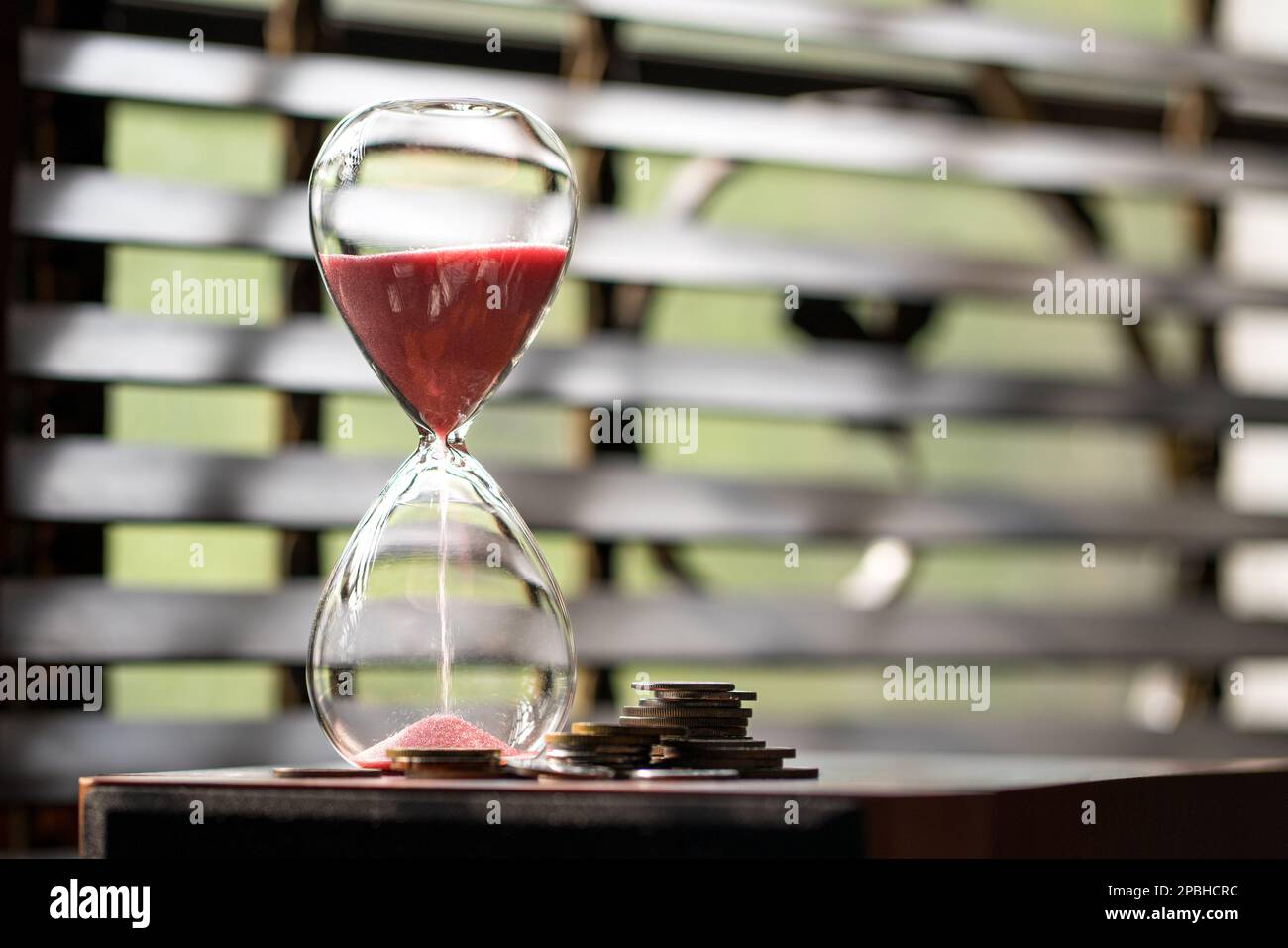 Sabbia che corre o che scorre giù di una clessidra con le monete accanto ad esso. Spazio di copia. Il tempo è concetto di denaro. Foto Stock