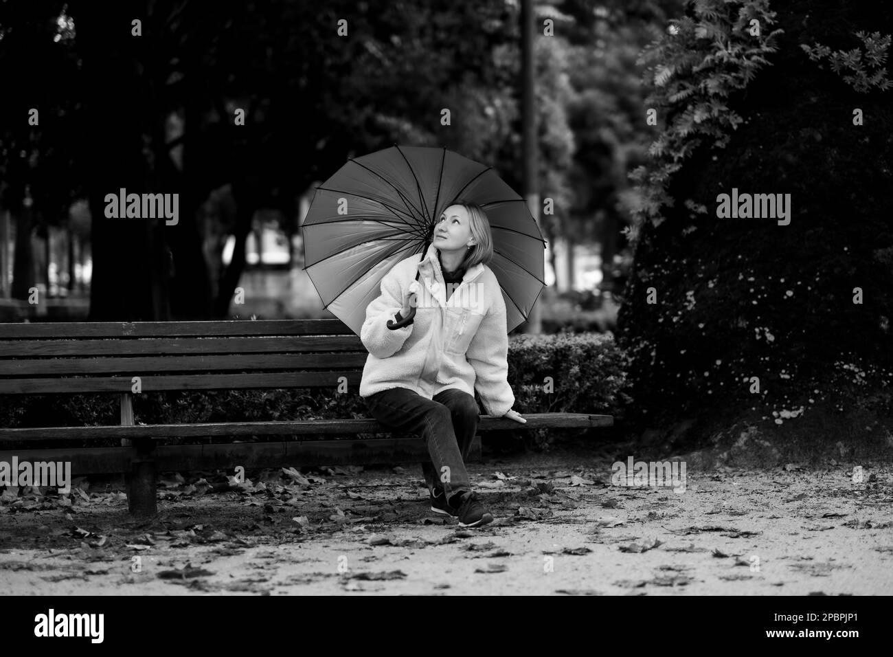 Una donna siede su una panchina del parco in caso di pioggia. Foto in bianco e nero. Foto Stock