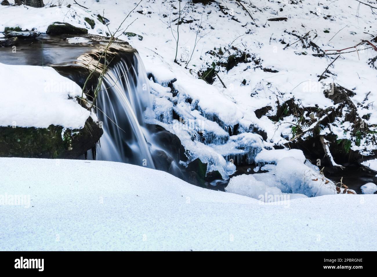 meravigliosa piccola cascata con ghiaccio e neve in un ruscello d'inverno Foto Stock