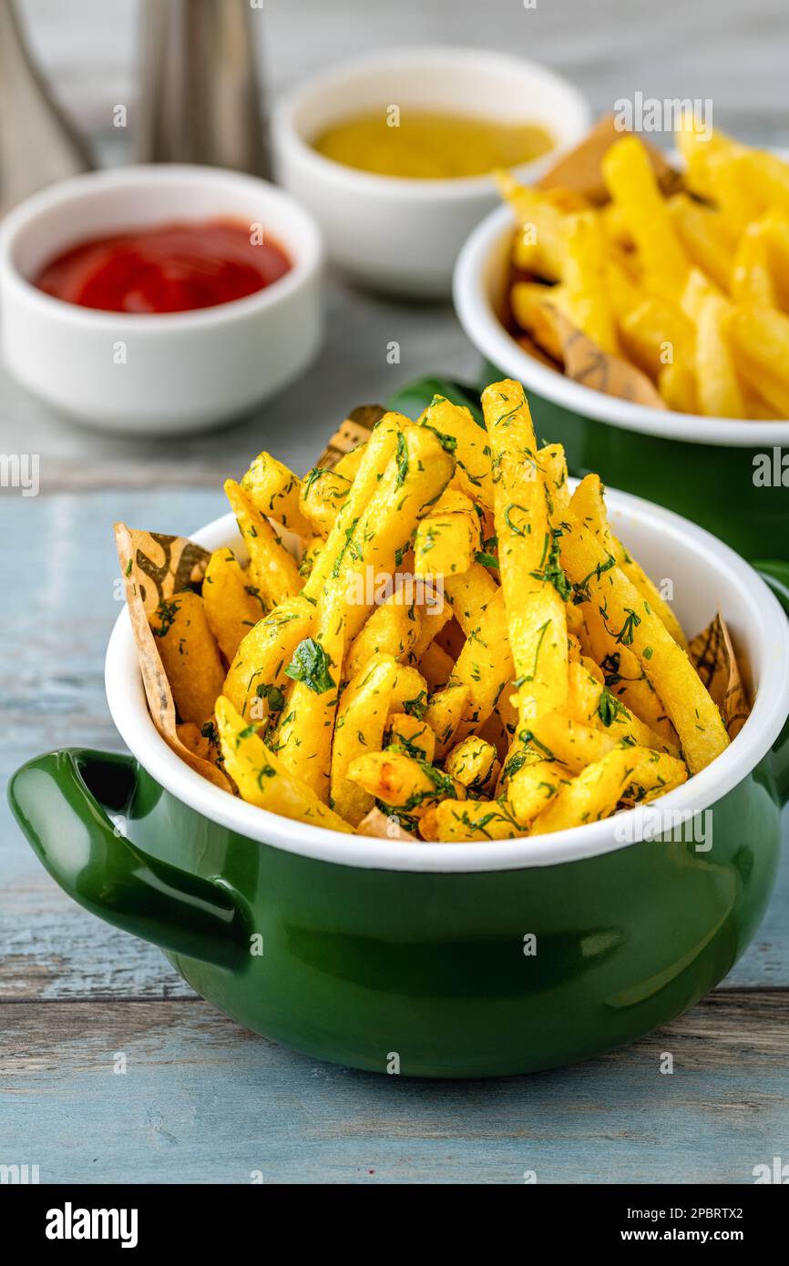 Fries francesi d'oro in una ciotola di smalto con salse varie sul lato Foto Stock