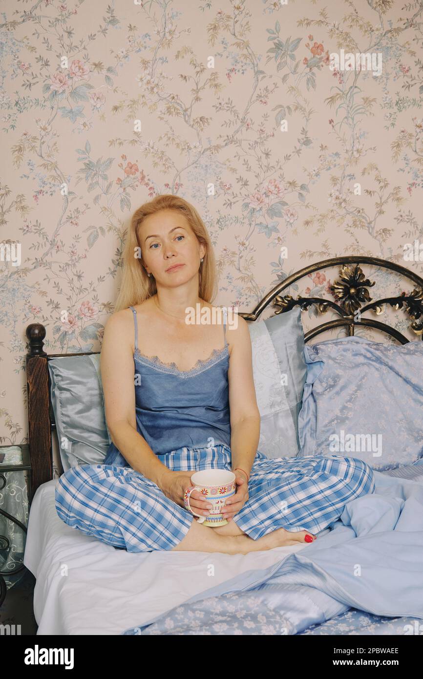 Donna di mezza età seduta in camera da letto gode mattina, bere caffè Foto Stock