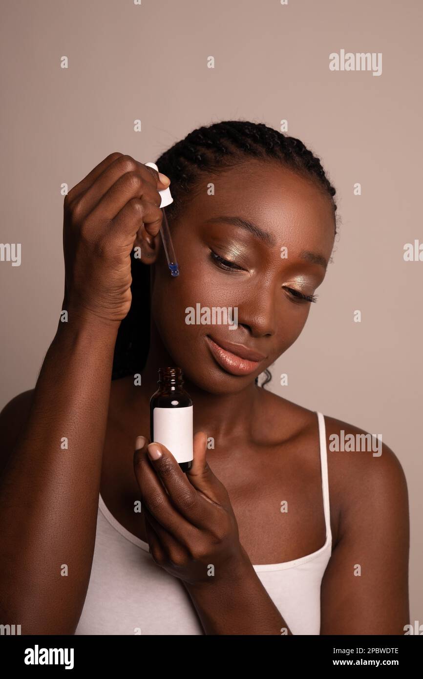 Modello femminile nero che applica il prodotto per la cura della pelle sul viso Foto Stock