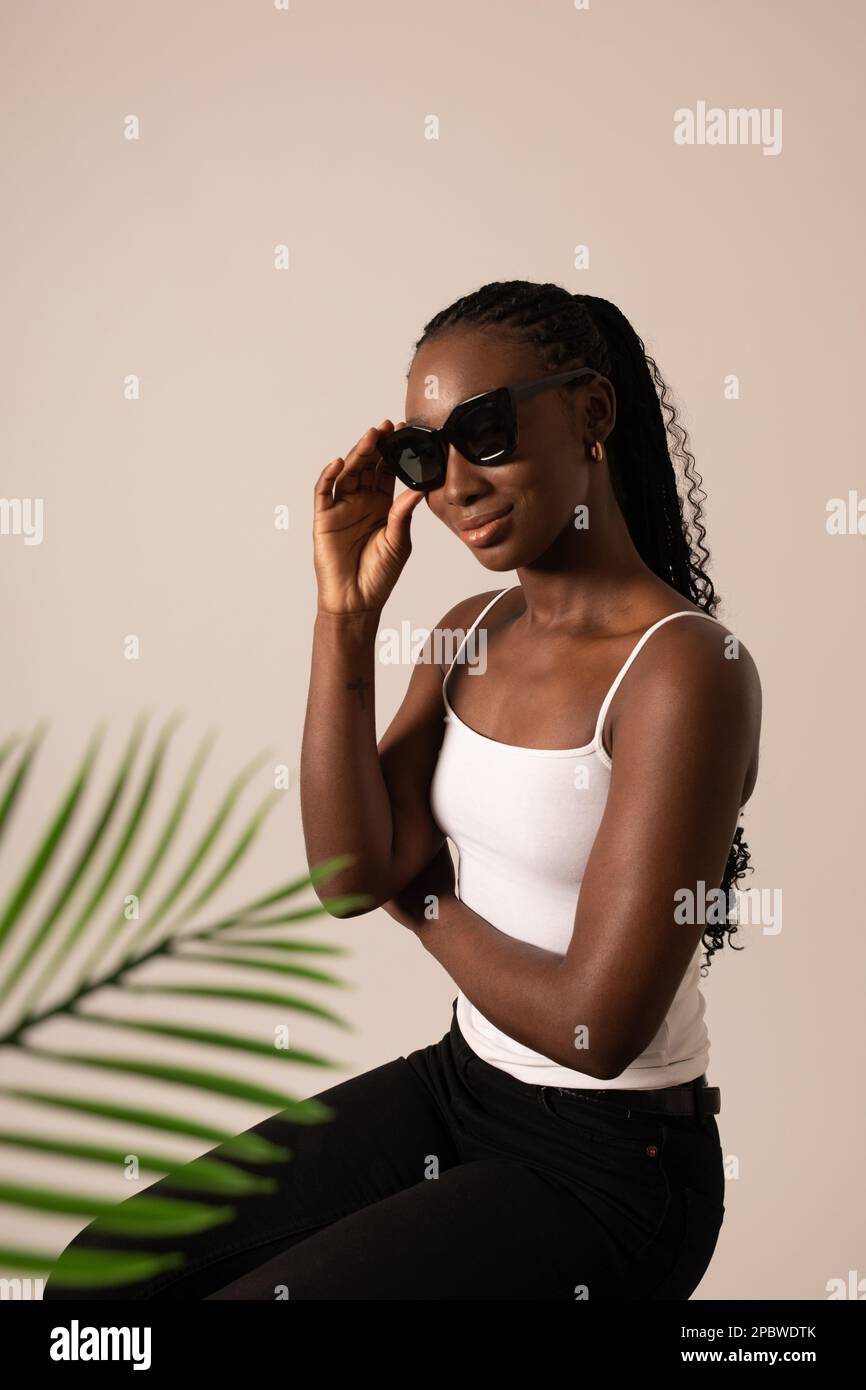 Modello nero femminile con occhiali da sole e una foglia di palma in studio Foto Stock