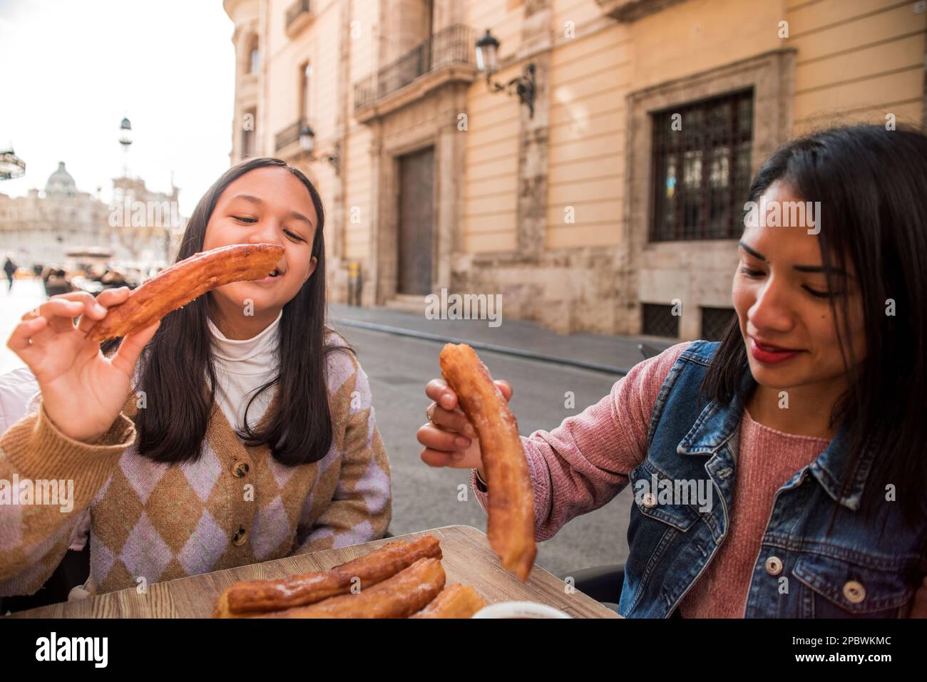 Giovane madre e figlia adolescente mangiano churros sulla terrazza del bar. Foto Stock