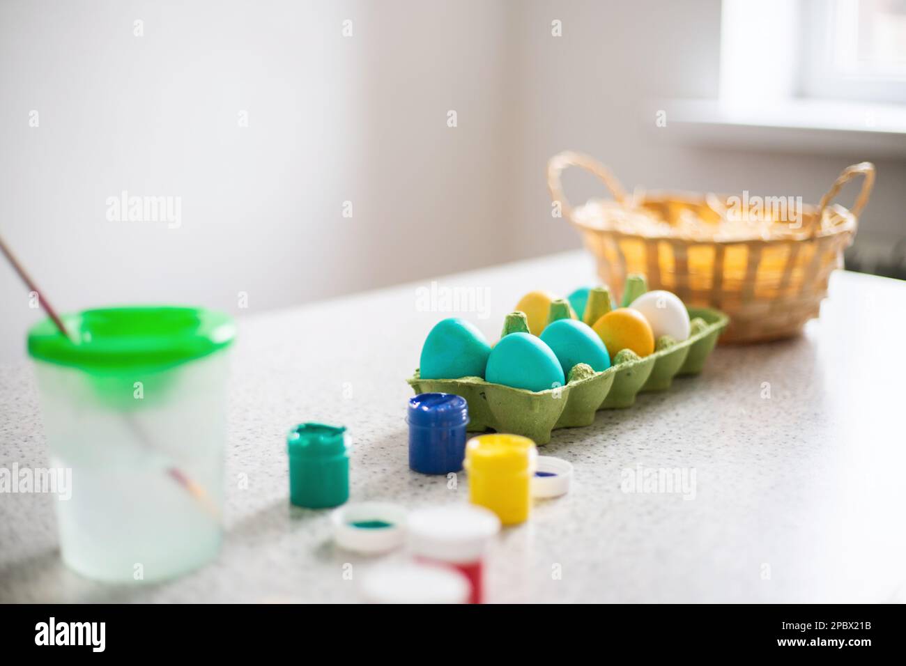 Uova già dipinte in tavola con pitture e cesto di vimini in una giornata di sole. Pasqua Foto Stock