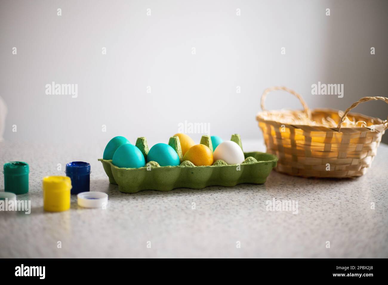 Uova già dipinte in tavola con pitture e cesto di vimini in una giornata di sole. Pasqua Foto Stock