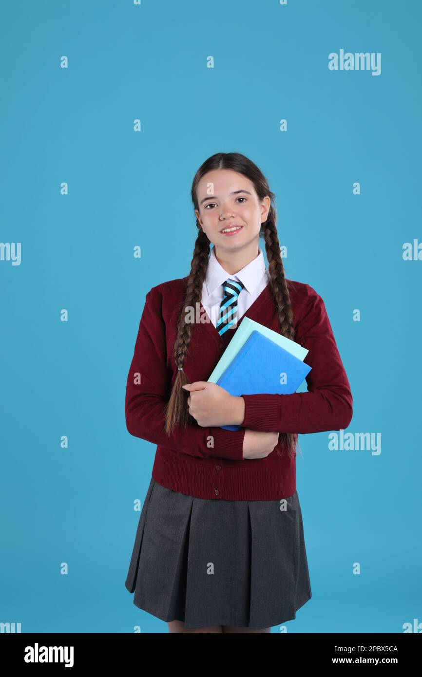 Ragazza adolescente in uniforme scolastica con libri su sfondo azzurro Foto Stock