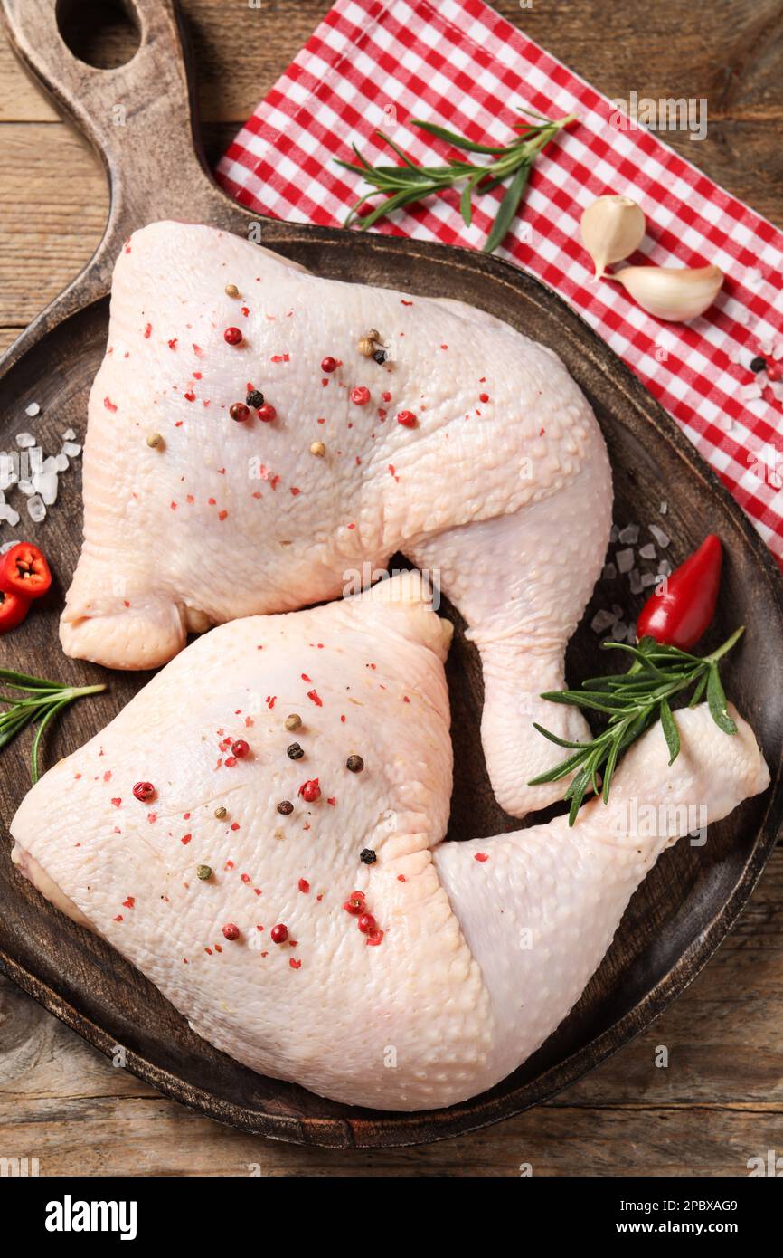 Quarti di coscia di pollo crudo e ingredienti su tavolo di legno, piatto Foto Stock