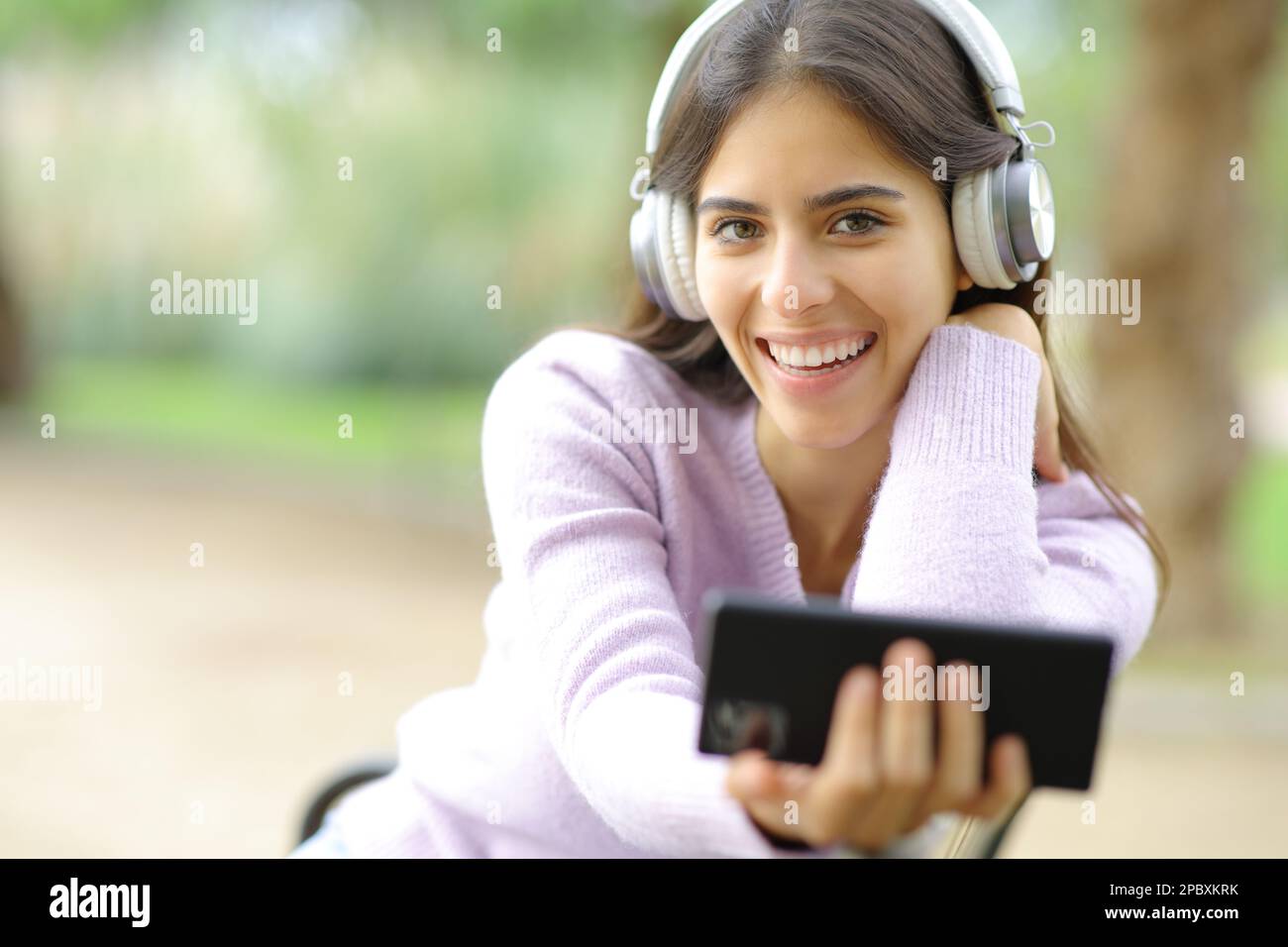 Donna felice ti guarda ascoltando musica in un parco Foto Stock